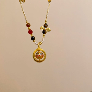 Close-up of golden rotating pearl pendant with red blue enamel and woven rope