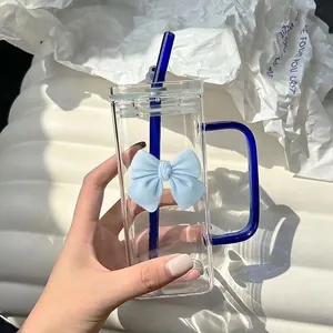 Close-up of square glass cup with blue handle, glass straw and blue 3D bow decoration