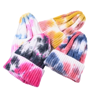 Detailed knit texture of four tie-dye beanie hats featuring thick cable knit patterns