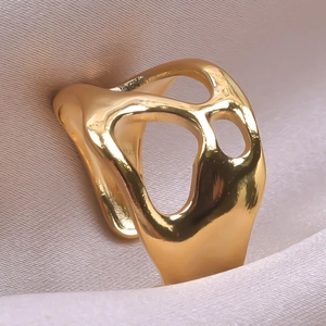 Detailed macro view of an irregular hollow gold-plated ring on soft champagne satin fabric