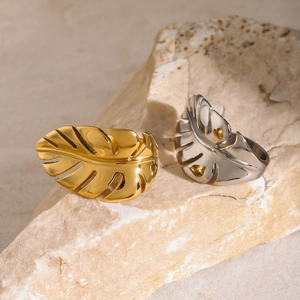 Polished 18k gold and silver monstera leaf rings on natural stone aesthetic display