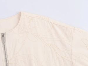 Close-up of floral embroidery and metallic zipper on a beige casual jacket