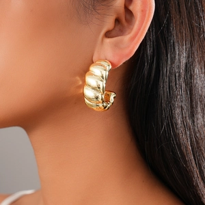 Detail of chunky gold-tone croissant hoop earring with spiral texture and polished finish