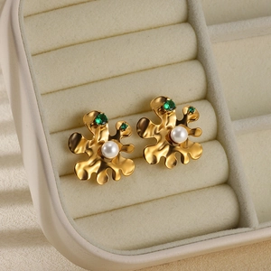 Macro view of gold-plated irregular earrings with pearls and green gemstones in a jewelry box