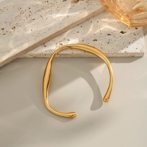 Detailed view of an irregular gold C-shaped titanium steel bracelet on travertine stone