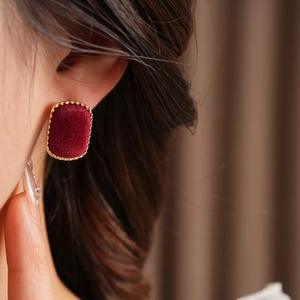 Close-up of model wearing rectangular burgundy velvet earrings with golden rope frames