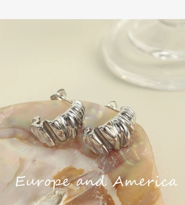 Detailed view of silver C-shape twisted hoop earrings placed on an iridescent shell