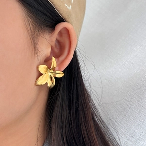 Close-up of a model wearing large 18K gold-plated floral stud earrings on white fabric