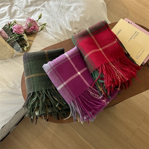 Plaid tassel scarves in dark green, purple and red displayed on a wooden tray