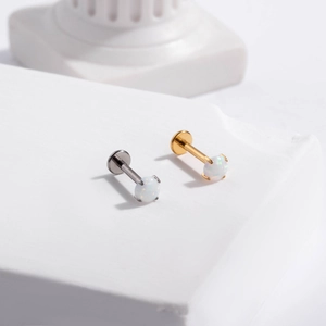 Macro detail of F136 titanium labret studs with opal stones on white pedestal