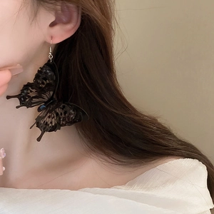 Detail of a large black acrylic butterfly earring with textured 3D wings on a model