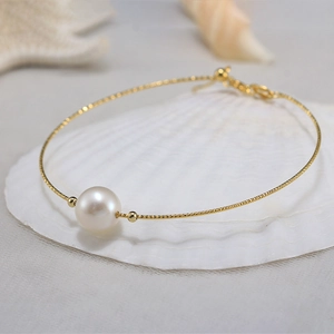 Macro shot of 14K gold plated silver chain with a natural white freshwater pearl on seashells