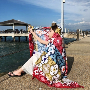 Ethnic red summer beach shawl worn by model on seaside boardwalk under blue sky and clouds