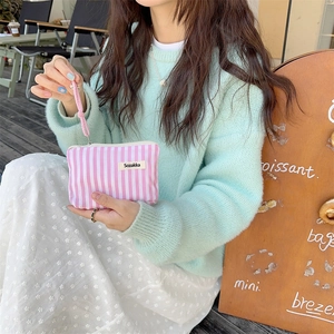 Pink striped cosmetic pouch held by hand in an outdoor cafe for a casual lifestyle look