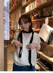Detail of soft black Y2k plush scarf with nice moment label on white knit vest