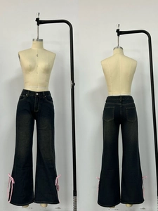 Dettaglio di jeans neri a zampa con fiocchi di nastro rosa sulle gambe laterali