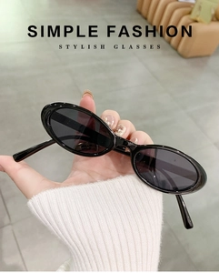 Detail of hand-held black oval narrow frame sunglasses with polished finish and dark lenses