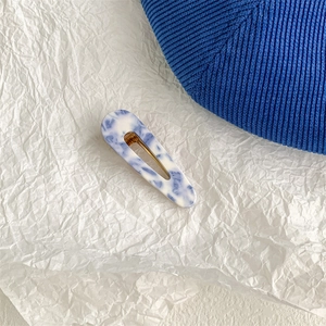 Close-up of blue and white marble-patterned drop-shaped hair clip with gold metal base