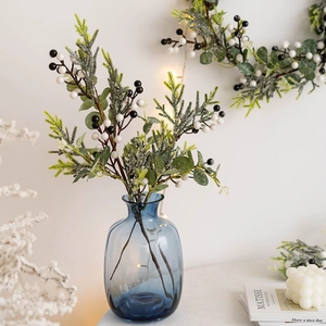 Festive Christmas wreath with green leaves and berries in a blue glass vase decor