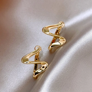 Macro shot of wavy gold-plated earrings on champagne silk, showcasing smooth mirror finish