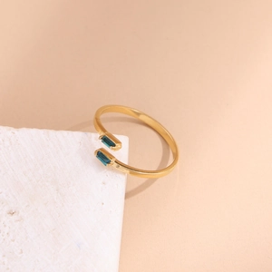 Detail of an asymmetric gold open ring with green rectangular gemstones on a stone base