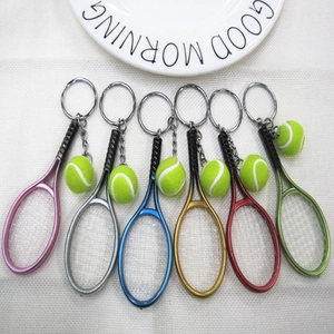 Detail view of six colorful mini tennis racket keychains with yellow balls on a fabric surface
