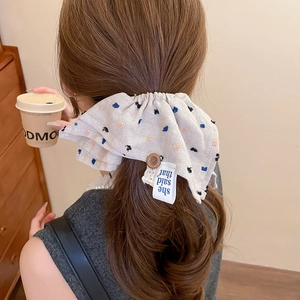 Close-up of beige floral pleated scrunchie with button detail and woven brand label