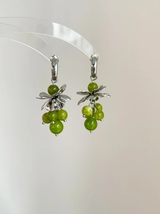 Close-up of silver C-shaped grape earrings with green beads and metallic leaf accents