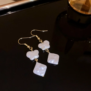 Detail view of pearl butterfly earrings with gold plating on a black reflective surface