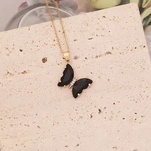 Détail du collier papillon doré avec ailes noires et diamants sur pierre beige