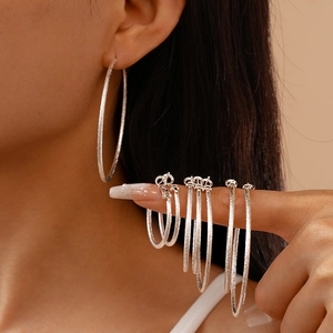 Silver geometric hoop earrings with matte glitter texture shown in various sizes on model