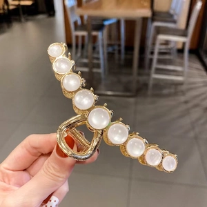 Detail of golden metal hair claw clip with elegant white pearls and a glossy finish