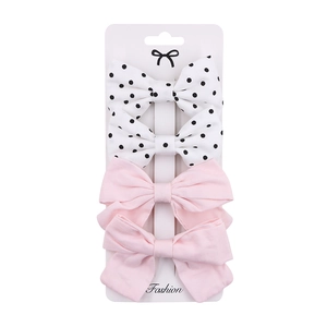 Detail of four fabric bow hair clips in pink and polka dot patterns on a white fashion card