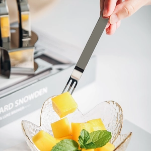Forchetta da frutta minimalista in acciaio inox 304 che raccoglie un cubetto di mango fresco