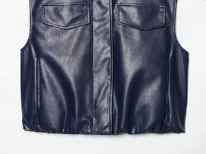 Detail of dark blue leather vest featuring utility pockets and gathered hemline texture