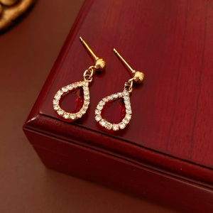 Detail of gold earrings with red teardrop stone and crystal halo on a wooden box