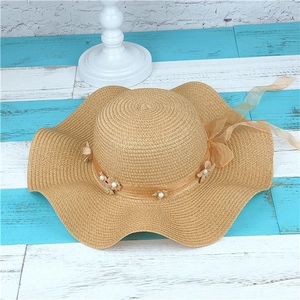 Close-up of woven straw hat featuring a wavy brim and organza floral lace with pearls