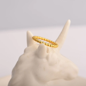 Minimalist golden perlee beaded wave ring displayed on a white ceramic unicorn statue