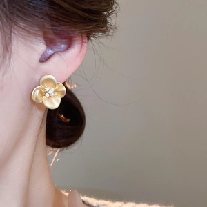 Close-up of matte gold flower stud earring with tiny zircons worn by a model