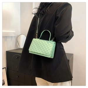Chic mint green crossbody bag with dark green M-pattern print worn over a black blazer