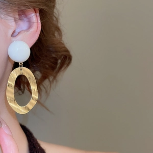 Macro view showing brushed metal texture and resin beads on oval drop earrings
