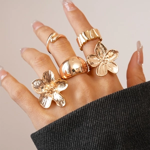Macro view of five-piece gold flower and geometric ring set worn on fingers