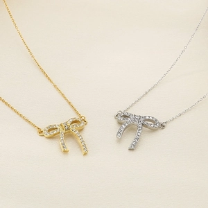 Detailed close-up of sparkling bow tie pendant necklaces in gold and silver steel finish