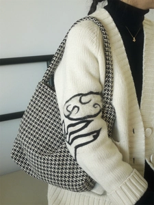 Detail of classic houndstooth tote bag styled with a minimalist cream knit cardigan
