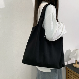 Grand sac cabas en toile noire avec lettrage blanc porté à l'épaule, style minimaliste