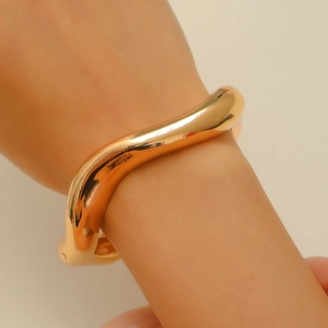 Close-up of golden irregular wavy open cuff bracelet with a polished metallic finish