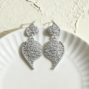 Detailed view of silver textured metallic drop earrings on a white ceramic plate