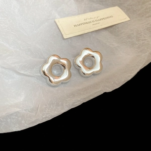 Détail de boucles d'oreilles fleurs argentées sur fond de papier blanc froissé