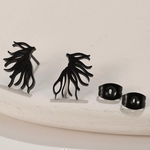 Detail of matte black tree branch earrings with butterfly backs on a stone texture