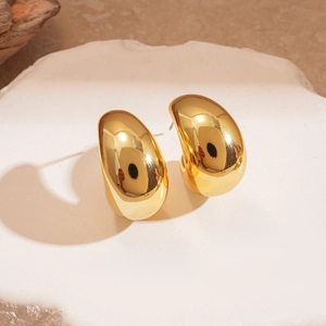 Detailed macro view of chunky golden drop earrings on textured white stone background